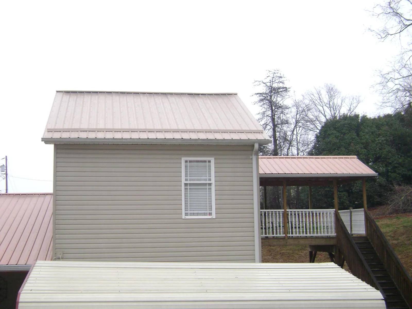 Tan metal roofs on a two story addition and attached porch, from a Roof Replacement job in Essex